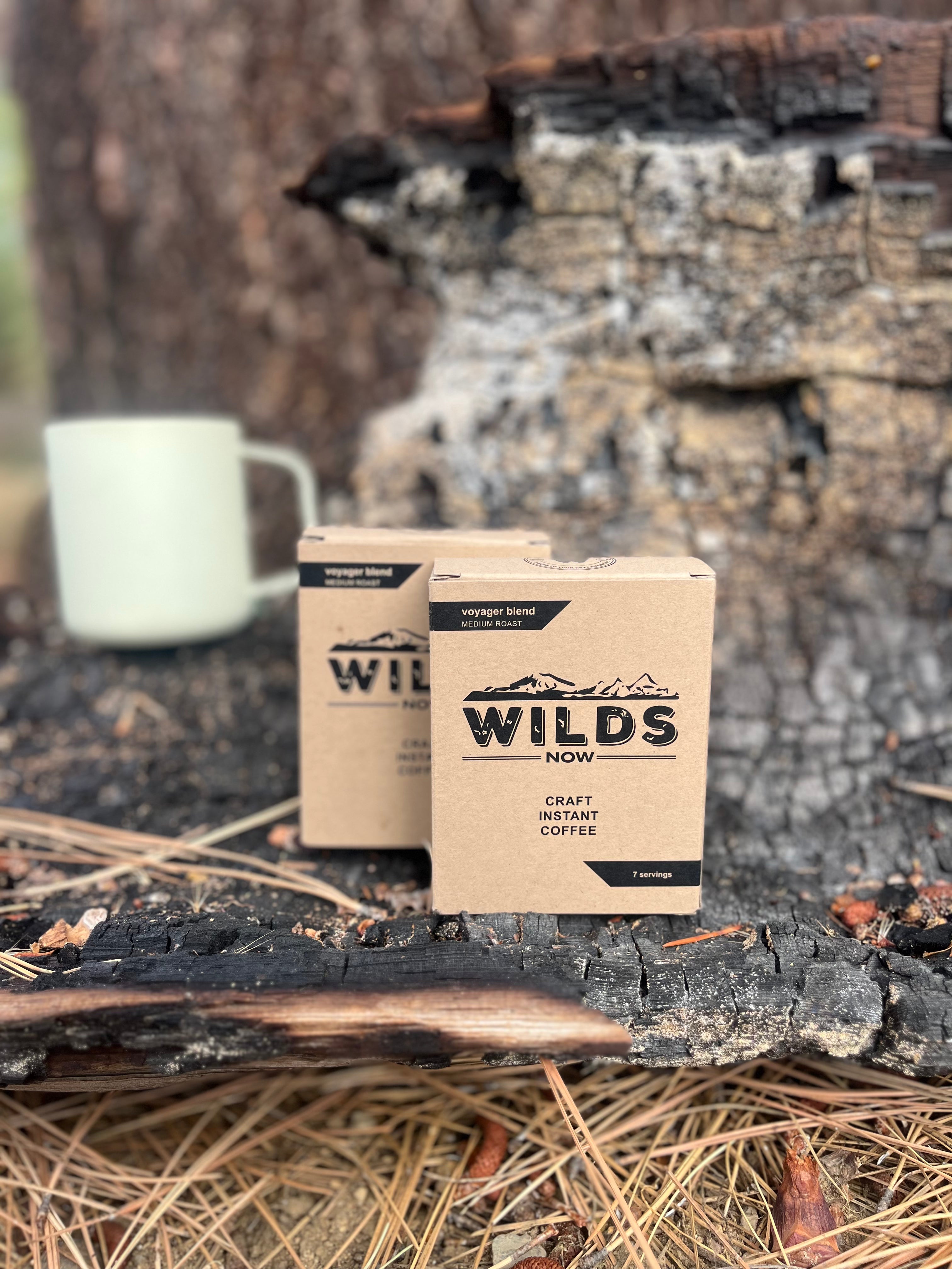 Two boxes of Wilds instant coffee on a wooden surface with a mug in the background.